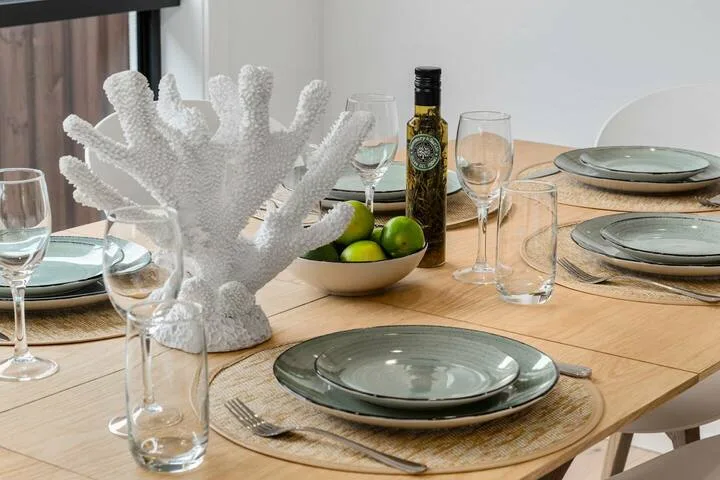 Una mesa de comedor está puesta con platos, vasos y un cuenco de fruta verde.