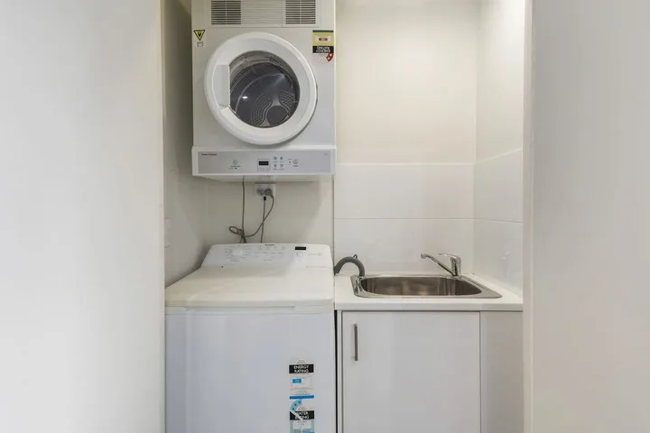 Zona de lavandería con lavadora y secadora apiladas junto a un fregadero.