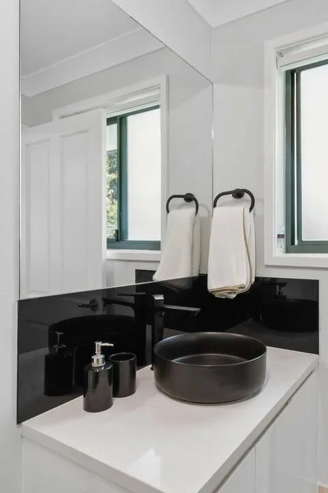 Un mueble de baño con un lavabo redondo oscuro está frente a un espejo grande.