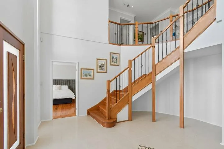 Interior luminoso con una escalera de madera, un descansillo superior y una puerta a un dormitorio.