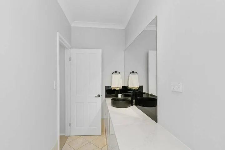 Un tocador de baño luminoso con una encimera larga, lavabos y un espejo grande.