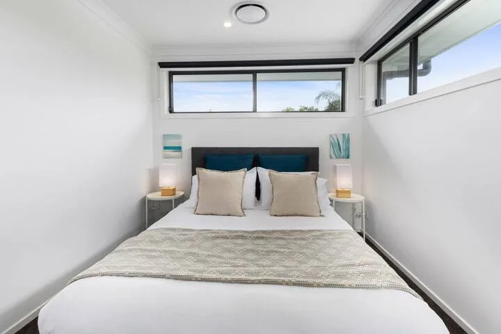 Un dormitorio luminoso con una cama bien tendida bajo ventanas amplias.