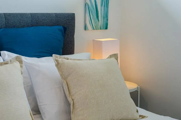 Un dormitorio con almohadas sobre la cama y una lámpara de mesita encendida.