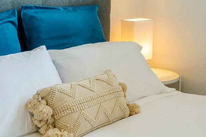 Un dormitorio con ropa de cama blanca, almohadas azules y una lámpara de noche.