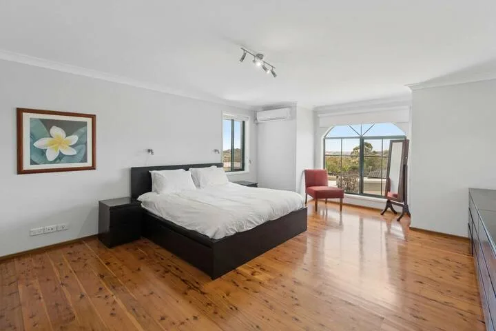 Un dormitorio luminoso con una cama grande, suelo de madera y puertas de vidrio que dan a un balcón.
