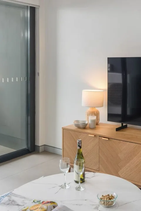 Una sala de estar con televisor, una lámpara encendida y una mesa de centro redonda.