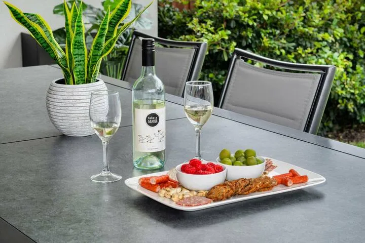 Una mesa de comedor al aire libre tiene vino, copas y un plato de aperitivos.