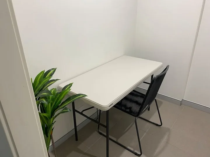 Una pequeña zona de reunión con una mesa blanca, asientos negros y una planta en maceta.