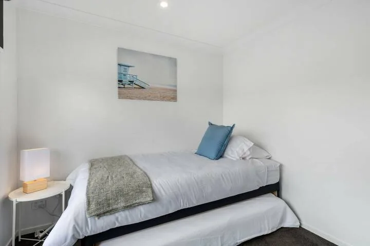 Un dormitorio blanco con una cama arreglada y un cojín azul.