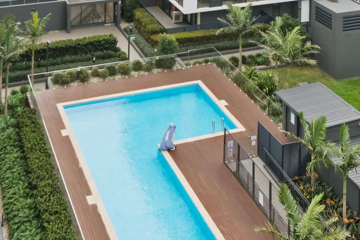 Una piscina al aire libre está rodeada por una terraza de madera y vegetación.