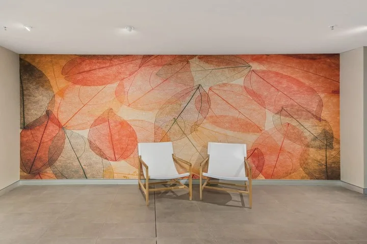 Dos sillas están frente a un gran mural abstracto en una sala luminosa.