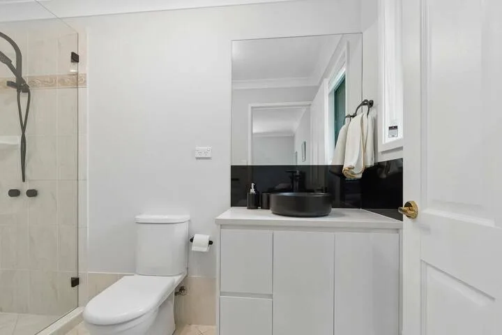 Un baño luminoso con lavabo, espejo, inodoro y ducha de vidrio.
