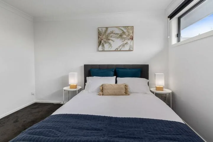 Un dormitorio luminoso con una cama tendida y un cuadro de palmeras.