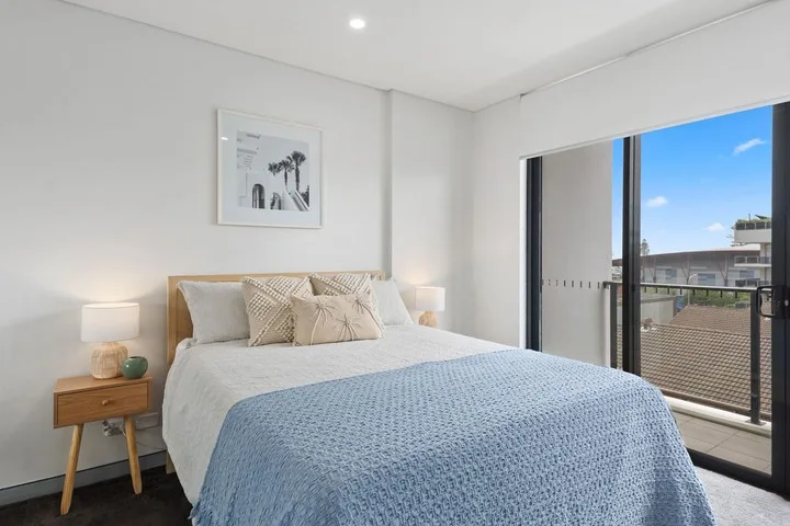 Un dormitorio luminoso con una cama bien arreglada y una puerta corrediza de vidrio que da a un balcón.