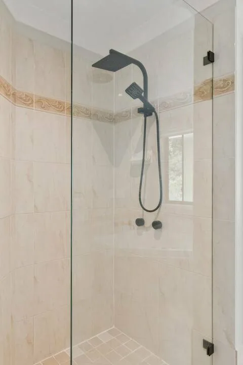 Una zona de ducha con azulejos, rociador oscuro y ducha de mano.