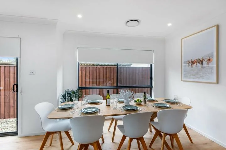 Comedor con una mesa de madera puesta con vajilla y rodeada de asientos blancos.