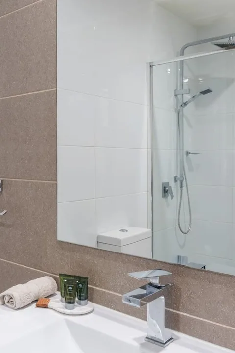 Un lavabo de baño con artículos de aseo junto a una ducha de vidrio.