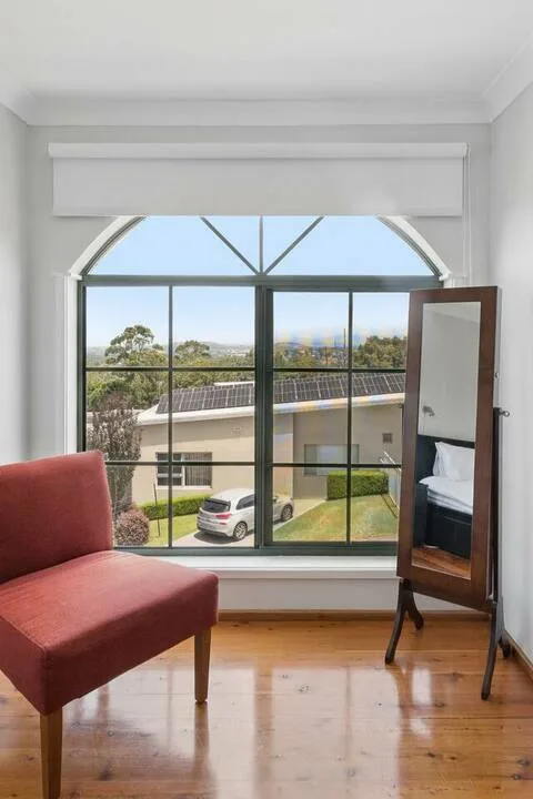 Un dormitorio luminoso con una gran ventana arqueada que da a casas y vegetación.