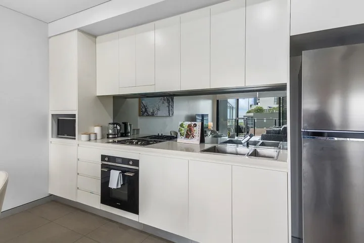 Una cocina moderna con armarios blancos, un horno empotrado y un refrigerador de acero inoxidable.