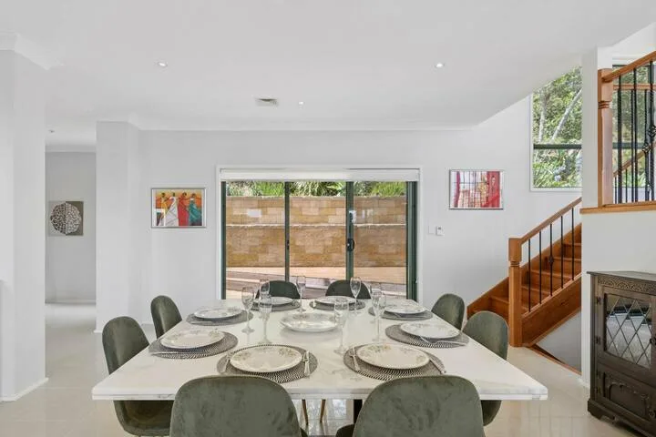 Comedor con una mesa larga puesta junto a grandes ventanas y una escalera.