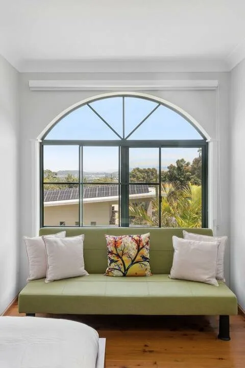 Un banco verde está debajo de una gran ventana arqueada con árboles al fondo.