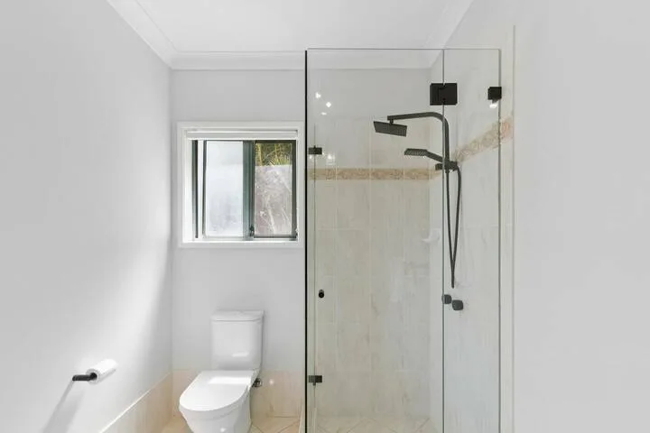 Un baño con ducha de cristal, inodoro y una ventana pequeña.