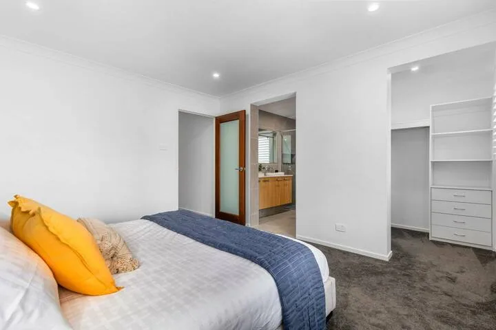 Un dormitorio luminoso con una cama y una puerta abierta hacia la cocina.