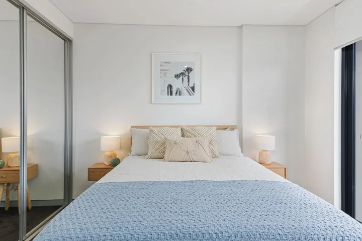 Un dormitorio luminoso con una cama bien arreglada y un cuadro sobre el cabecero.