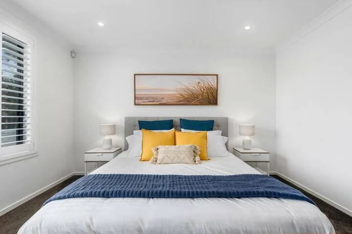 Un dormitorio luminoso con una cama bien arreglada y un cuadro de paisaje sobre el cabecero.