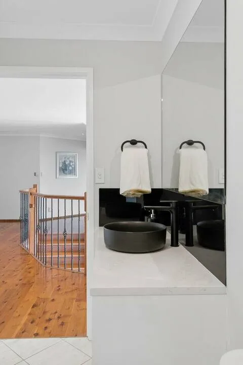 Un lavabo de baño con una pila sobre encimera y un espejo grande junto a un pasillo con suelo de madera.