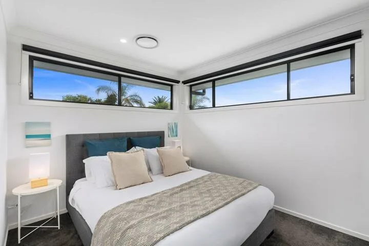 Un dormitorio luminoso con una cama bajo amplias ventanas en esquina.