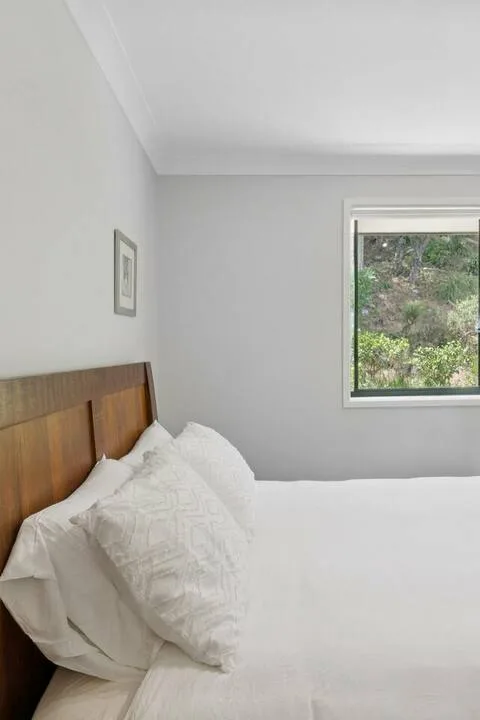 Un dormitorio con ropa de cama blanca y una ventana con vistas a la vegetación.
