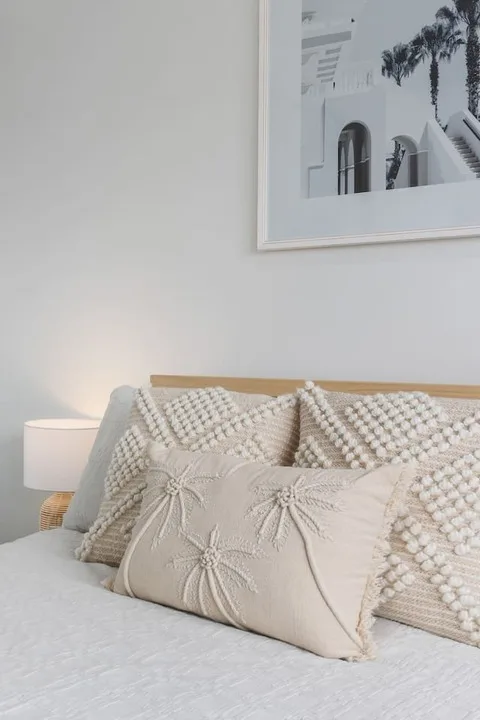 Una cama de dormitorio está decorada con cojines texturizados bajo un cuadro enmarcado.