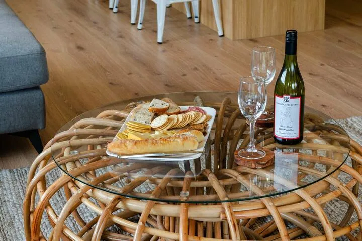 Una zona de estar con una mesa de centro de vidrio preparada con aperitivos y vino.