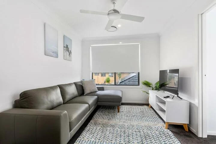 Una sala luminosa con sofá en L, alfombra estampada y televisor.