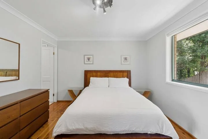 Un dormitorio luminoso con una cama bien tendida y una ventana con vista a la vegetación.