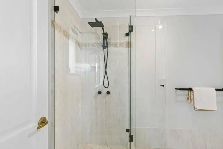 Una ducha de baño con azulejos, cabezal oscuro y toallero fijado a la pared.