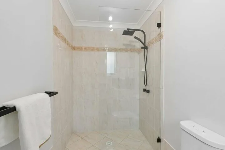 Zona de ducha en un baño alicatado, con una ventana pequeña y ducha de pared.