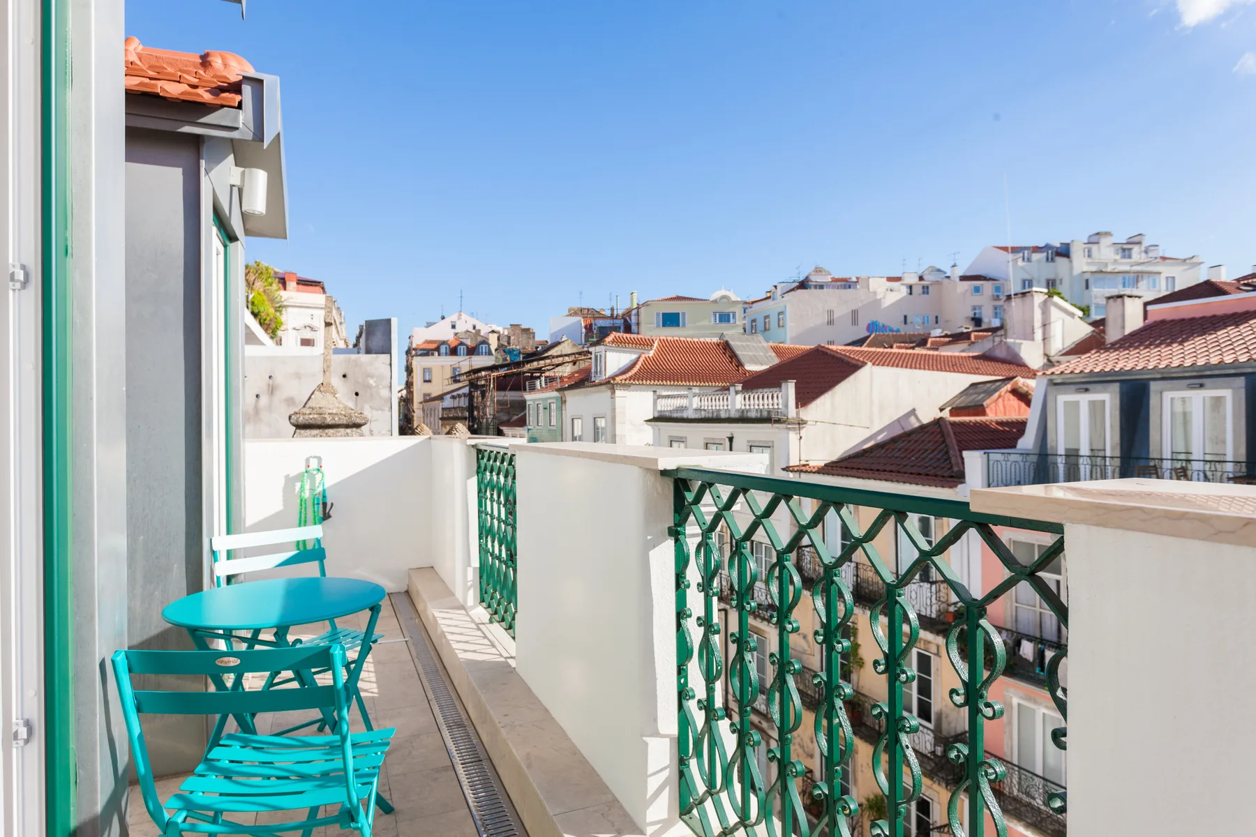 A sunny balcony overlooks nearby buildings and rooftops.