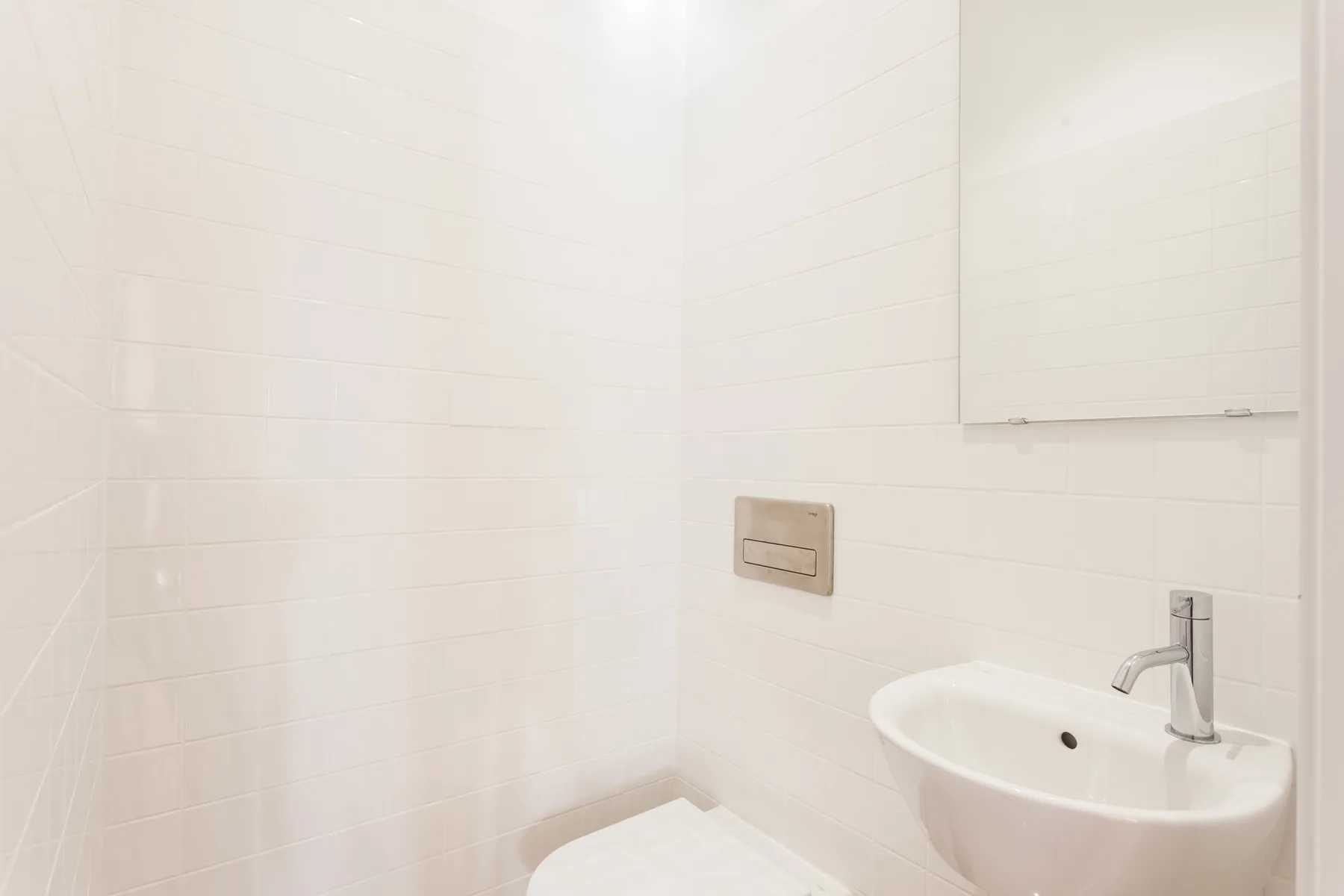 A bright bathroom with a wall-mounted flush plate and sink.
