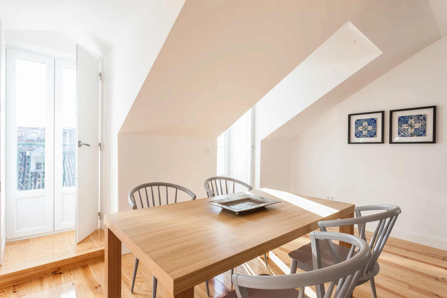 A dining area with a wooden table and chairs beneath a sloped ceiling.