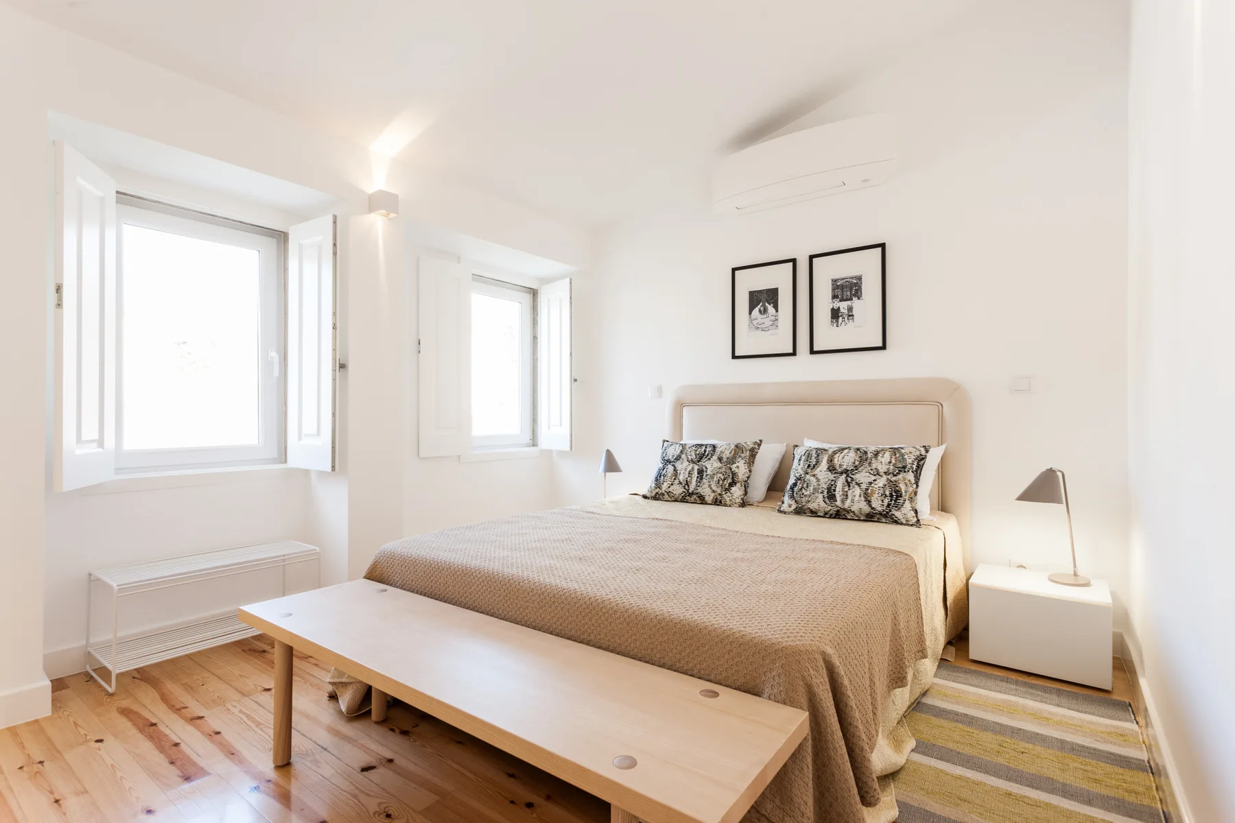 Un dormitorio luminoso con una cama, una mesa baja y ventanas.
