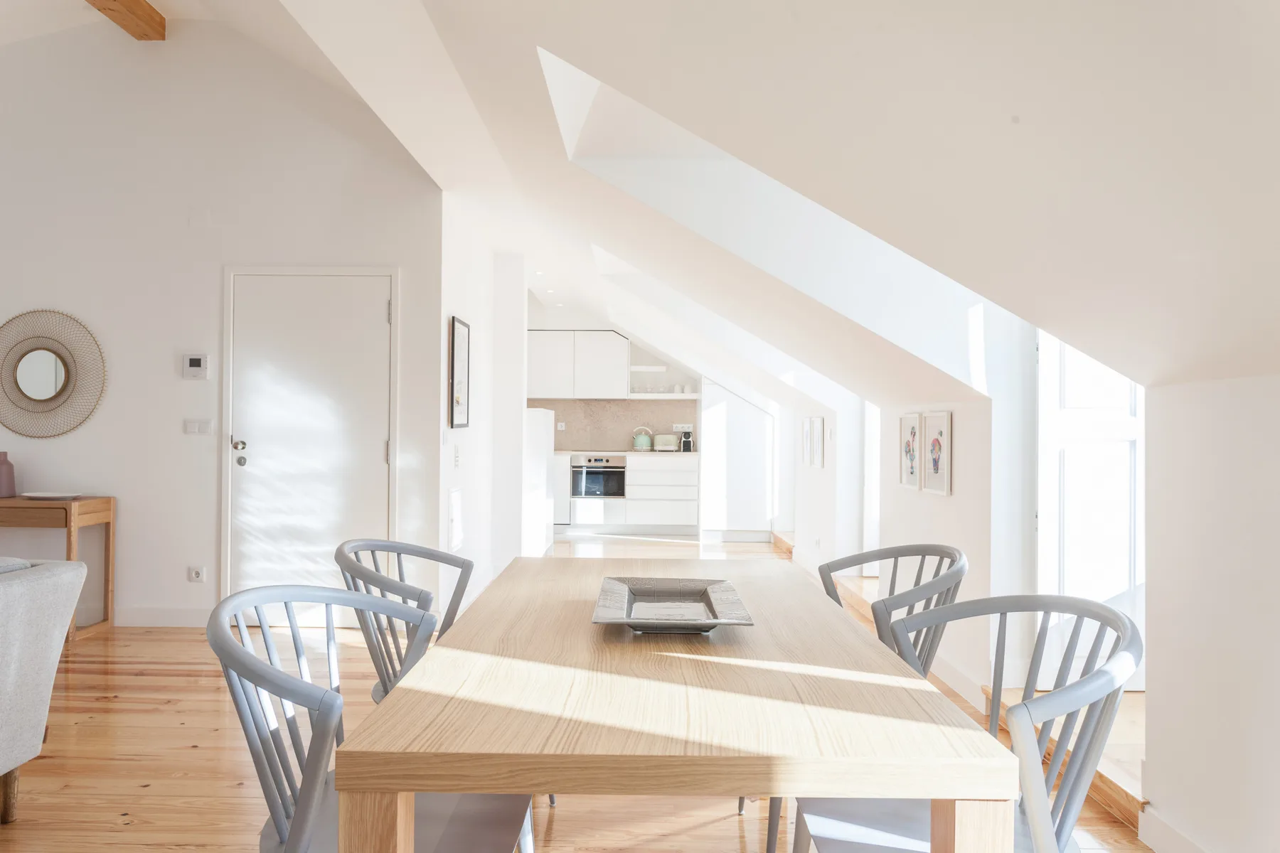 A bright dining area has a long wooden table and chairs beneath a sloped ceiling.