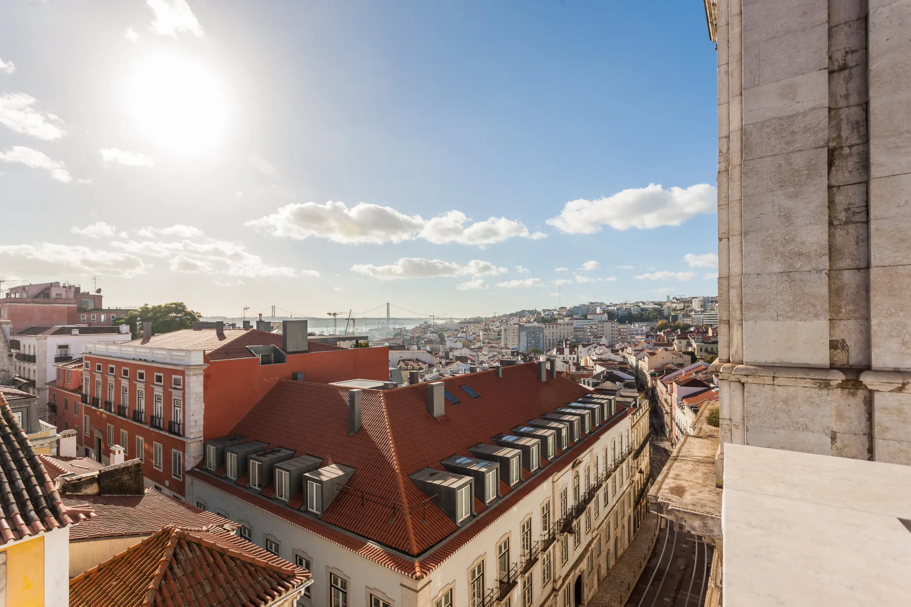 Rooftop city view with red-tiled buildings beneath a bright sky.