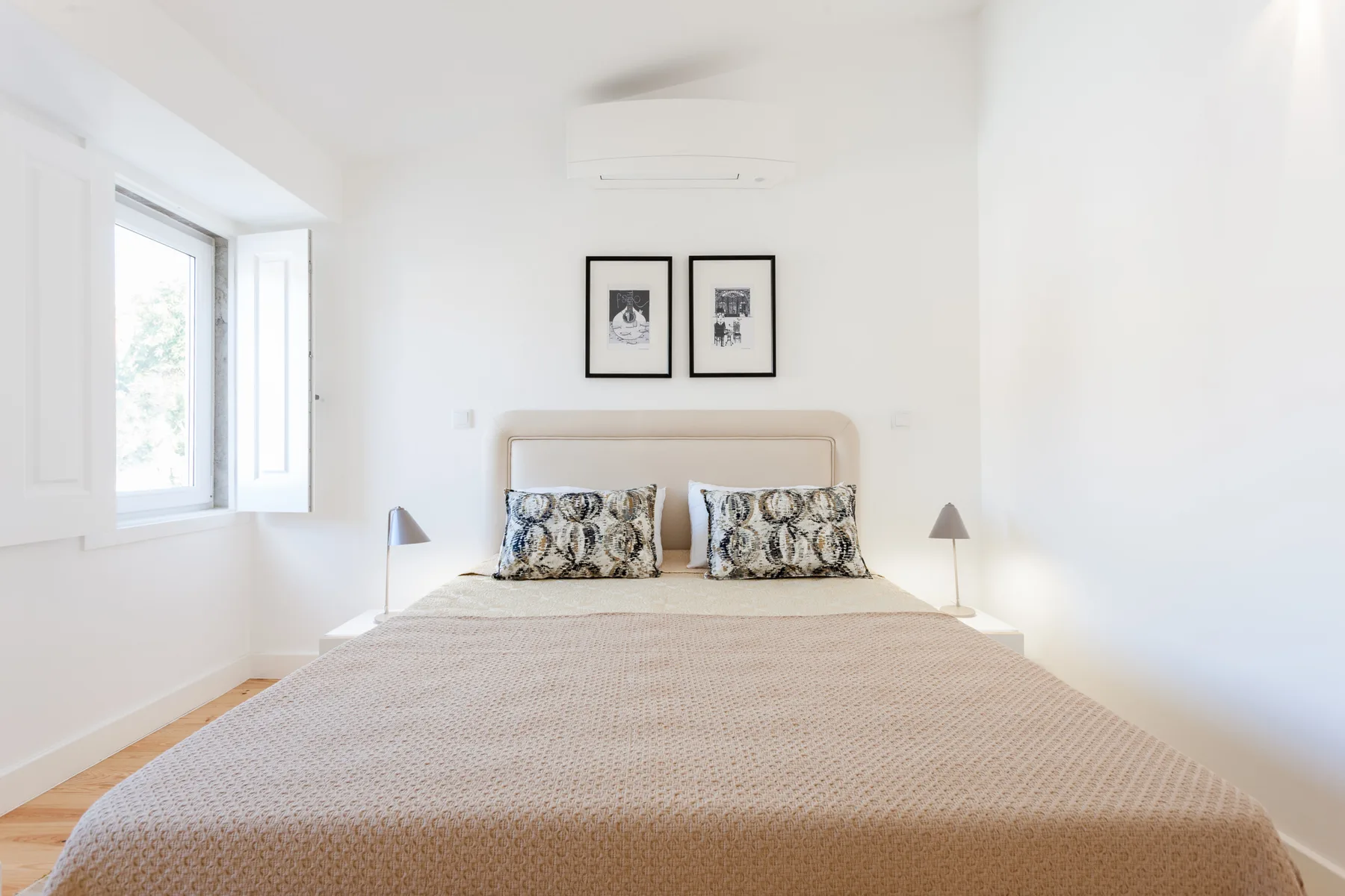 A bright bedroom with a bed, bedside lamps, and an open window.