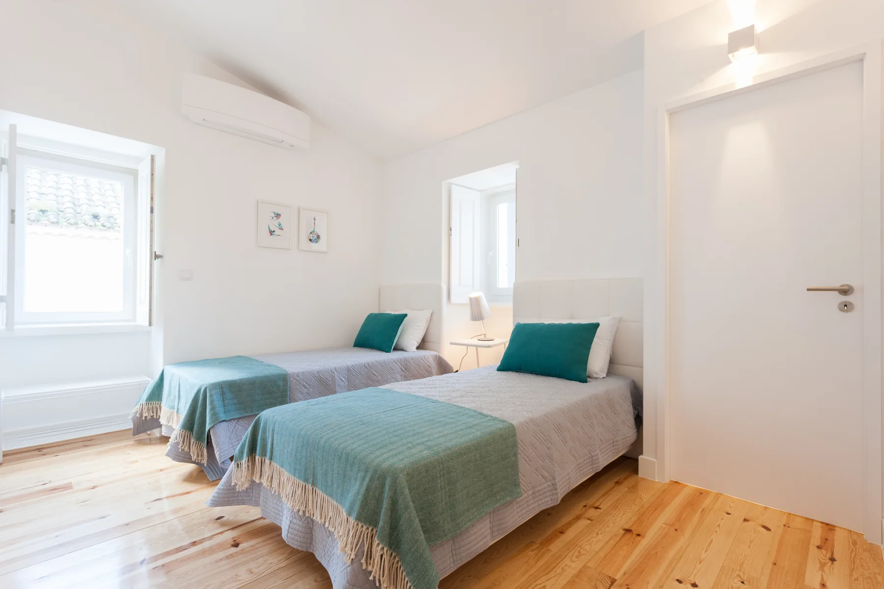 Un dormitorio luminoso con dos camas cubiertas de ropa de cama color turquesa.