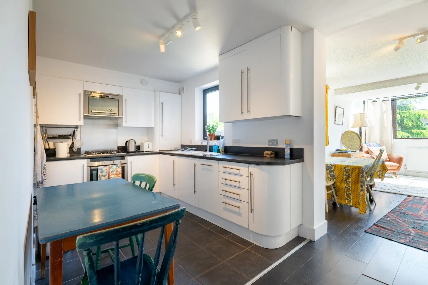 A bright kitchen with white cabinets, dark countertops, and a dining table.