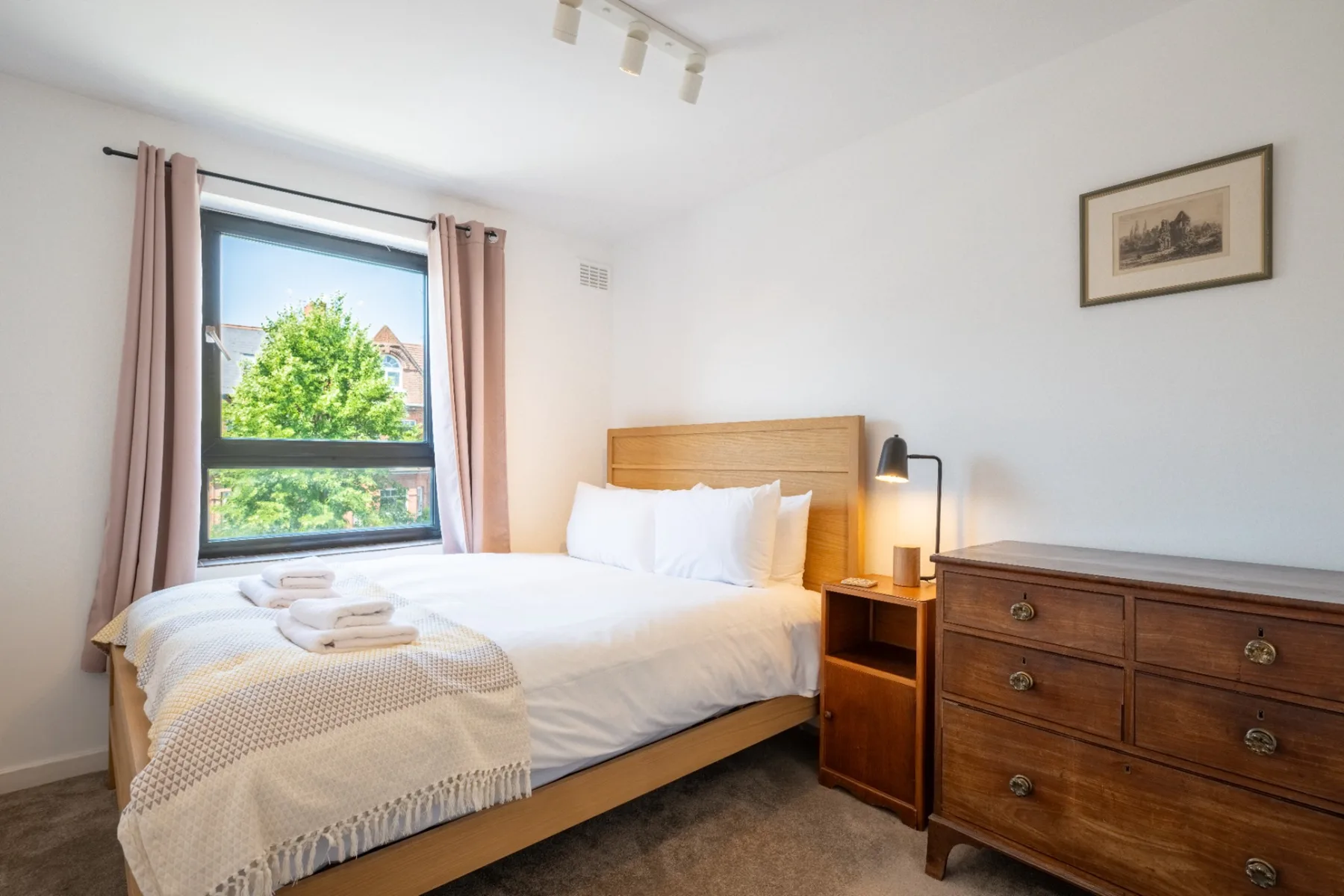 A bright bedroom with a wooden bed, bedside table, and window.