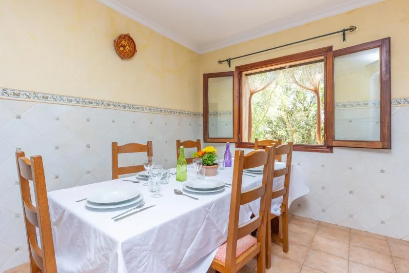 Un comedor con una mesa puesta junto a una ventana abierta.