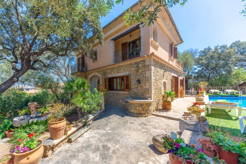 Una casa de piedra y estuco se alza junto a un patio pavimentado con flores de colores.
